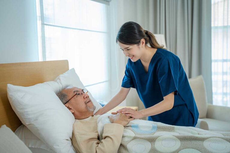 An adult child sits quietly beside a senior parent, holding hands and sharing a moment of reassurance in a home setting.