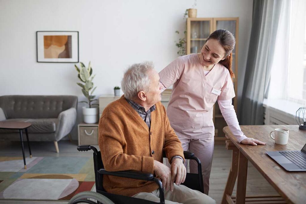 Caregiver helps an older resident wash hands beside a clean assisted living bathroom sink.